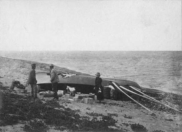 Two men and one women on beach with supplies and overturned boat