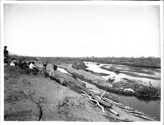 Group of Pima Indian farmers sitting on shore looking at an irrigation ...