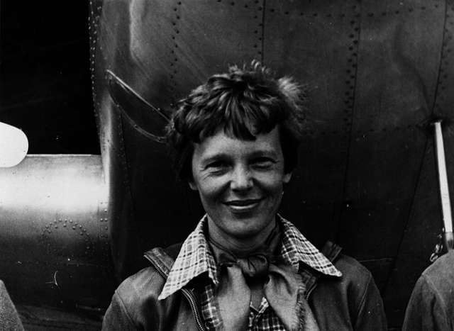 Amelia Earhart standing under nose of her Lockheed Model 10-E Electra ...