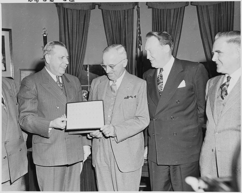 Photograph of President Truman in the Oval Office receiving a sheet of ...