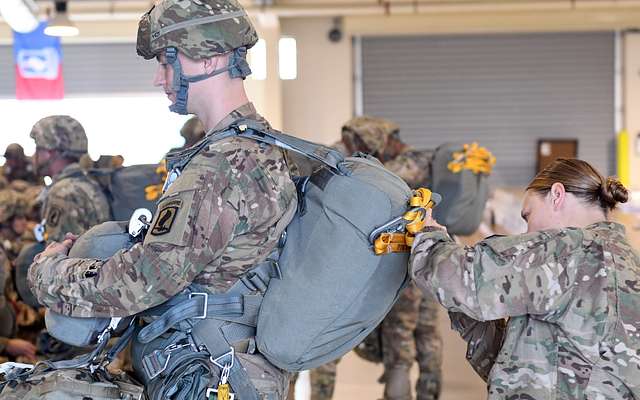 A jumpmaster receives a static line from a paratrooper during mock