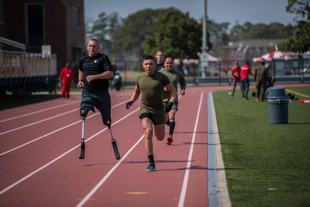 four men, one with prosthetic legs, run together on a track