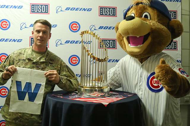 A U.S. Army Soldier's son poses with Clark, the Chicago Cubs mascot, at the  USO at USAG Bavaria in Grafenwoehr, Germany, Dec. 11, 2018. The USO  sponsored a Chicago Cubs mascot tour